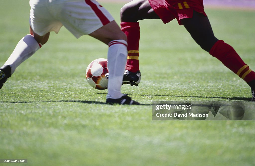 Two male soccer players with ball, low section (Digital Enhancement)