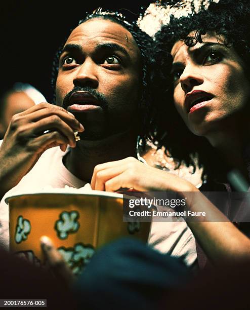 man and woman in theater eating popcorn - kinosaal stock-fotos und bilder