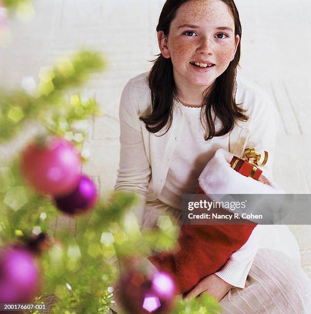 girl (8-10) holding christmas stocking beside christmas tree, smiling - stocking tops stock pictures, royalty-free photos & images