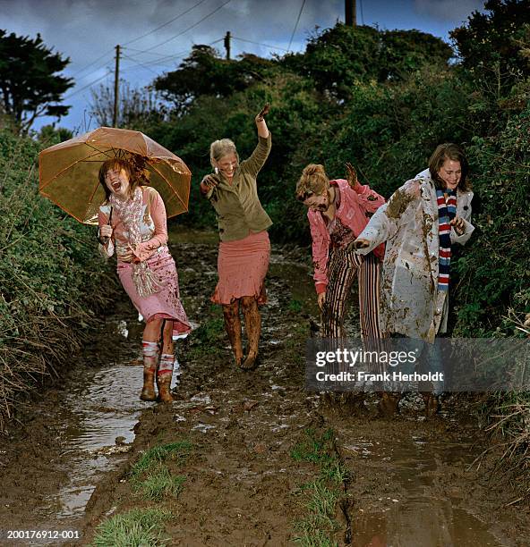 four young women having mud fight outdoors, laughing - schlammschlacht stock-fotos und bilder