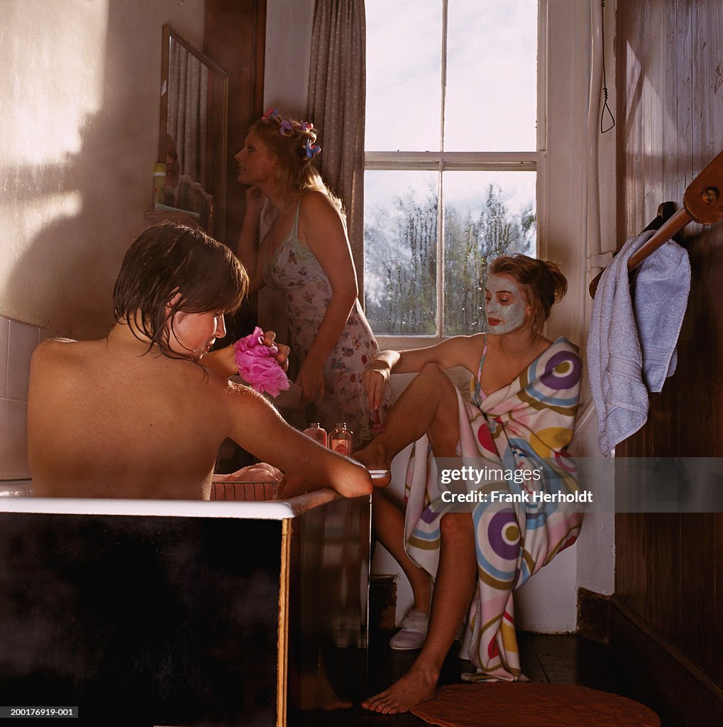 Three young women in bathroom, woman in bath in foreground