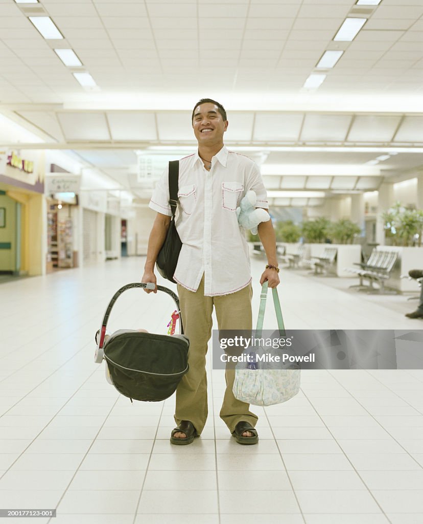 Young man carrying baby carriage and bags in airport