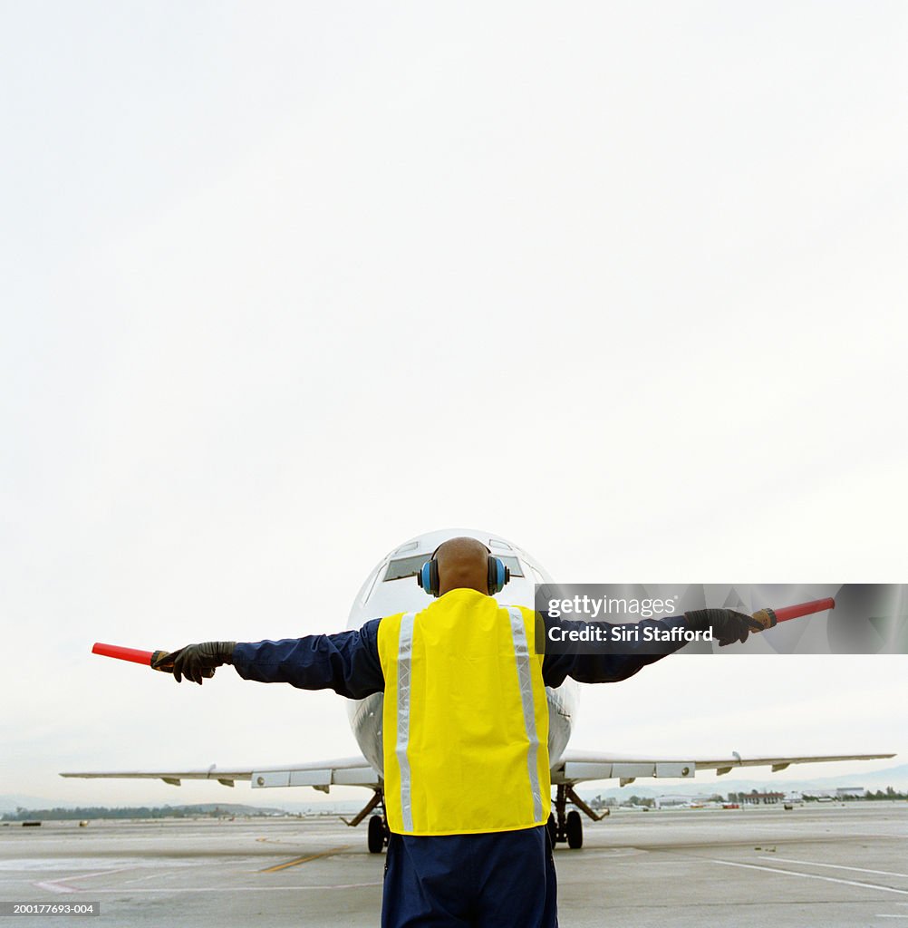 Airport ground crew directing aircraft, rear view