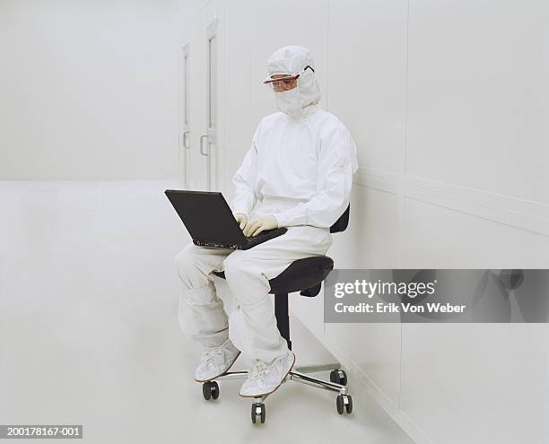 lab technician on chair using laptop - mono blanco traje protector fotografías e imágenes de stock
