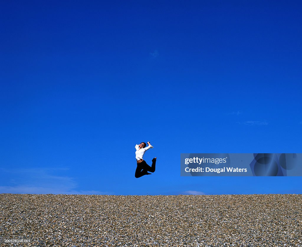 Young woman jumping on pebbled beach