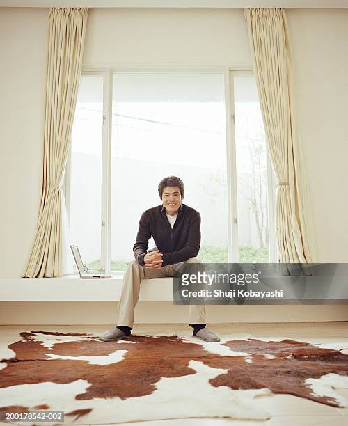 young man sitting on window ledge next to laptop, portrait - pantalon beige photos et images de collection