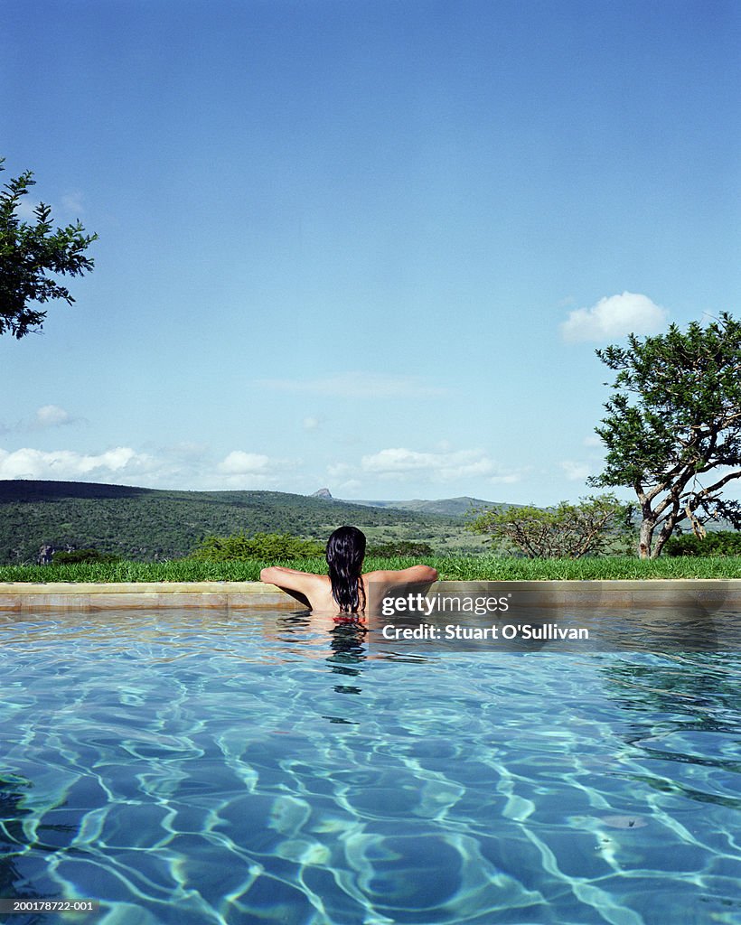 Woman at edge of swimming pool looking at view, rear view