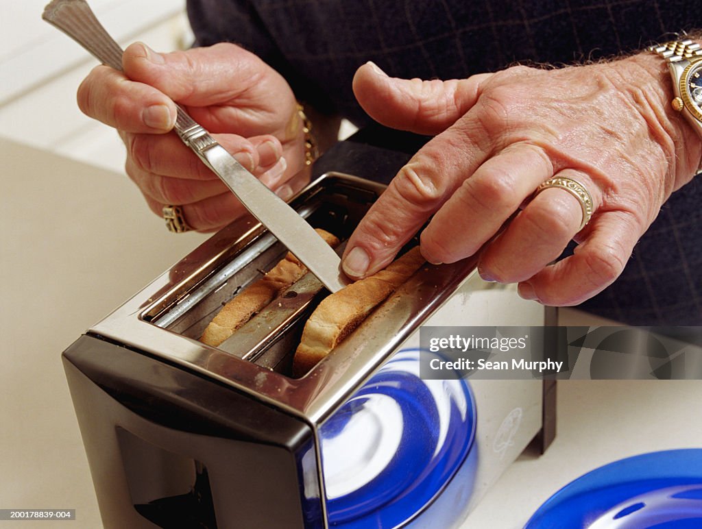 Senior man getting toast out of toaster with knife, close-up