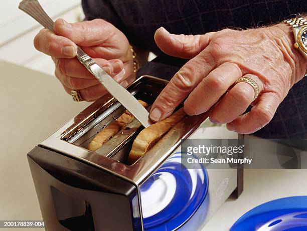 senior man getting toast out of toaster with knife, close-up - careless stock pictures, royalty-free photos & images