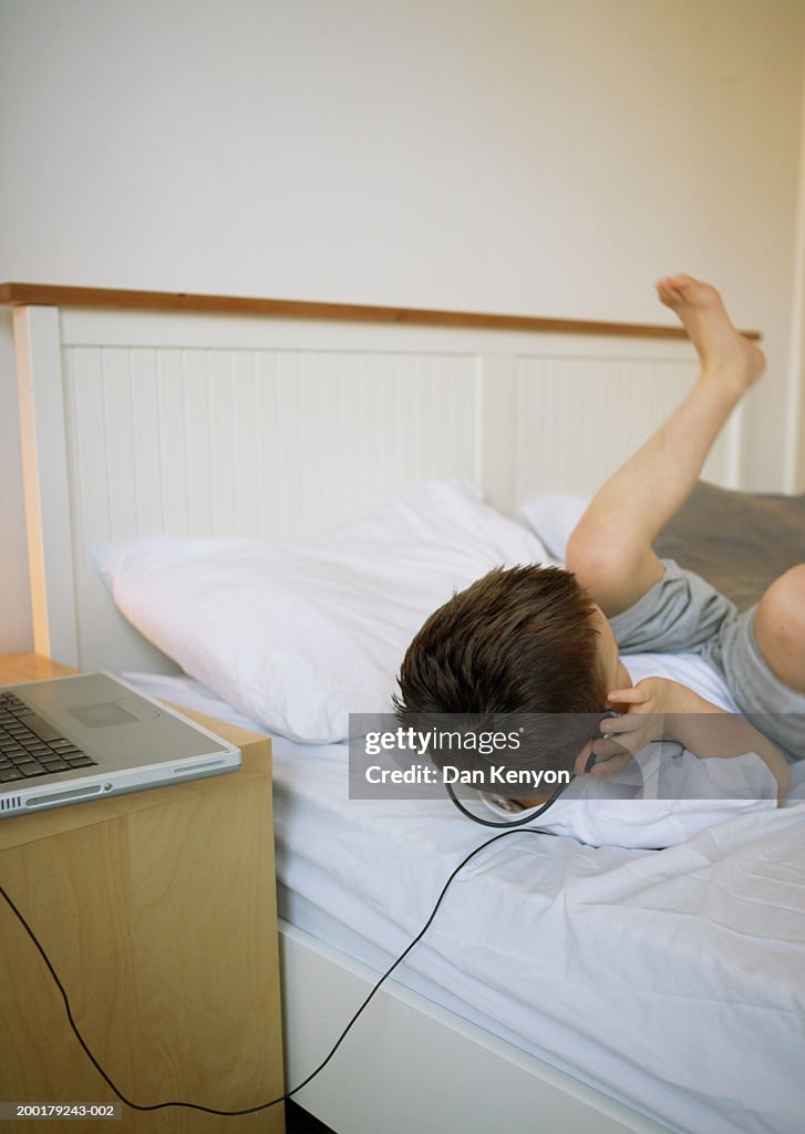 Boy (4-6) lying on bed wearing headphones