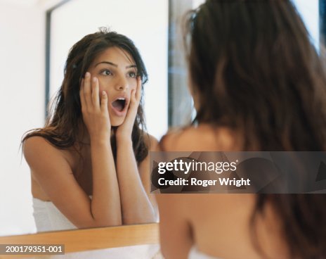 Young woman looking at reflection, hands on cheeks Young woman looking at reflection, hands on cheeks