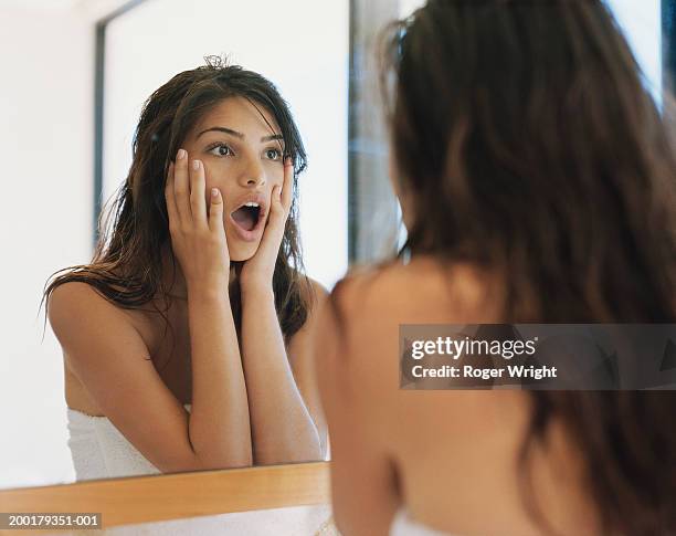 young woman looking at reflection, hands on cheeks - black hair imagens e fotografias de stock
