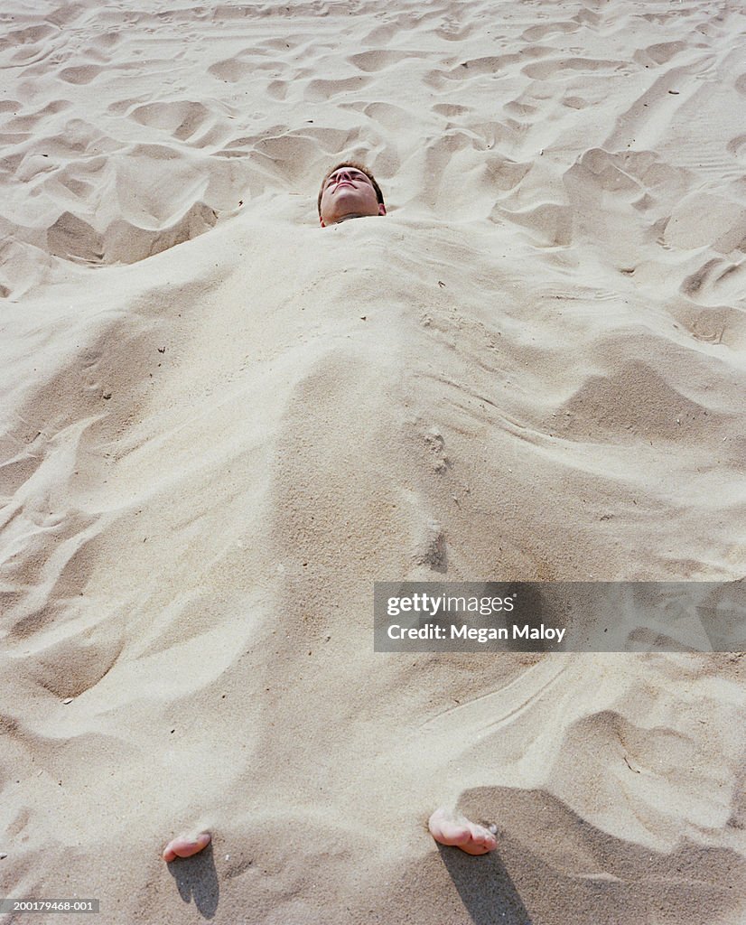 Man buried in sand on beach with eyes closed, elevated view