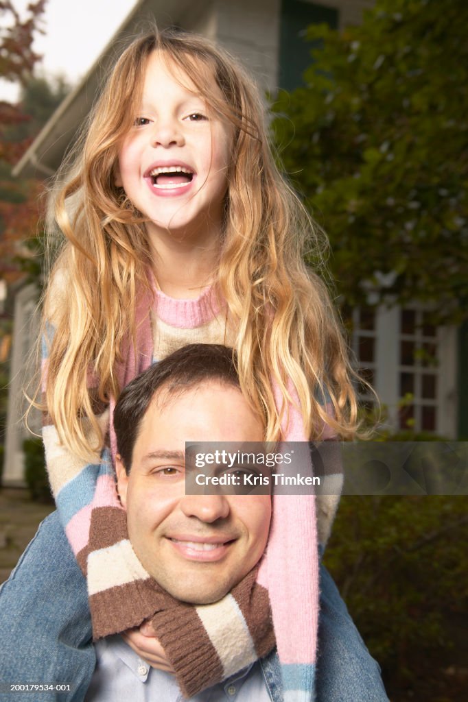 Girl (5-7) sitting on father's shoulders, portrait