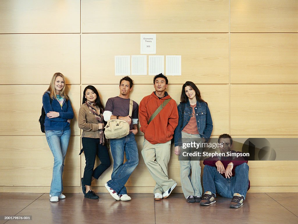 Group of college students standing against wall, grades posted above