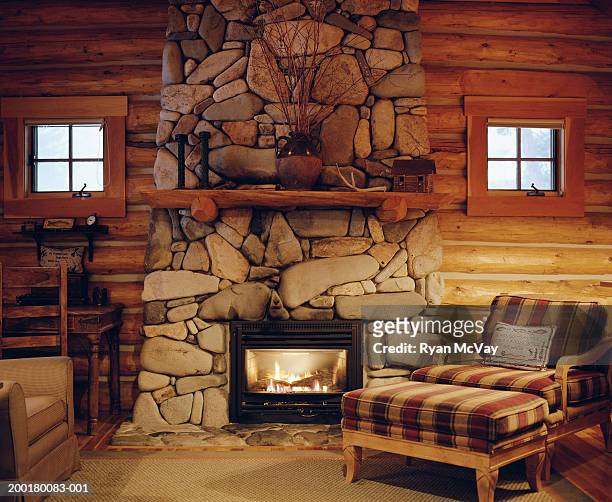 armchair beside stone fireplace in log cabin - cabin stockfoto's en -beelden