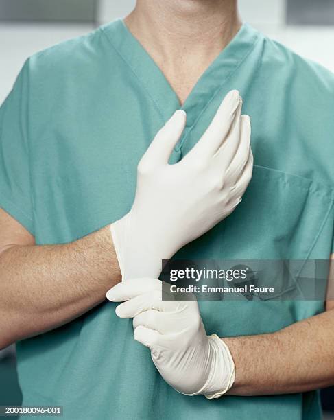 surgeon putting on latex gloves, mid section - grüner handschuh stock-fotos und bilder