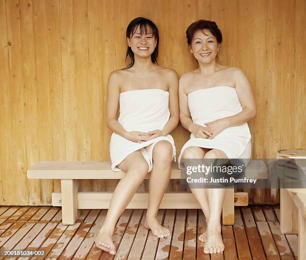 two women wrapped in towels sitting on wooden bench, smiling, portrait - envuelto en una toalla fotografías e imágenes de stock