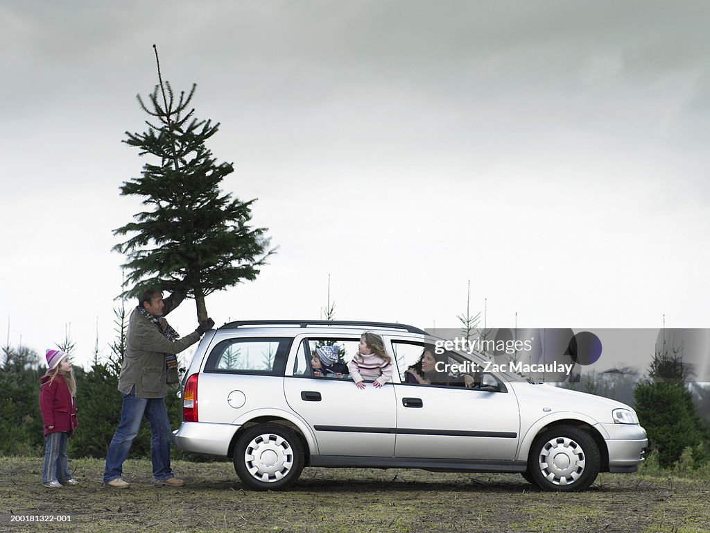 Family loading Christmas tree onto roof of car