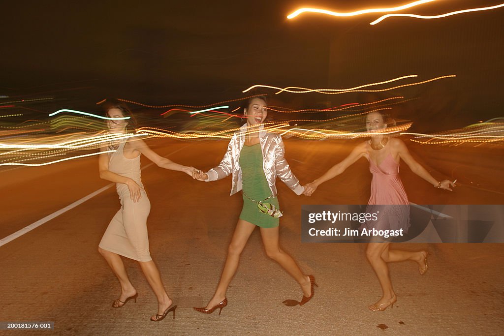 Three young women crossing street at night, side view (long exposure)