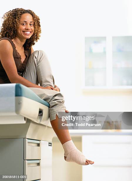 young woman with bandaged foot sitting on examination table, portrait - ankle sprain imagens e fotografias de stock