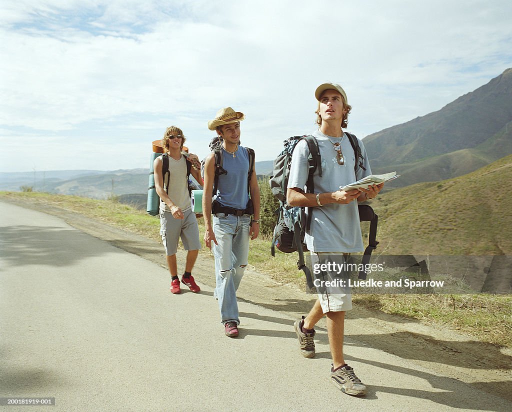 Three young male backpackers walking along road