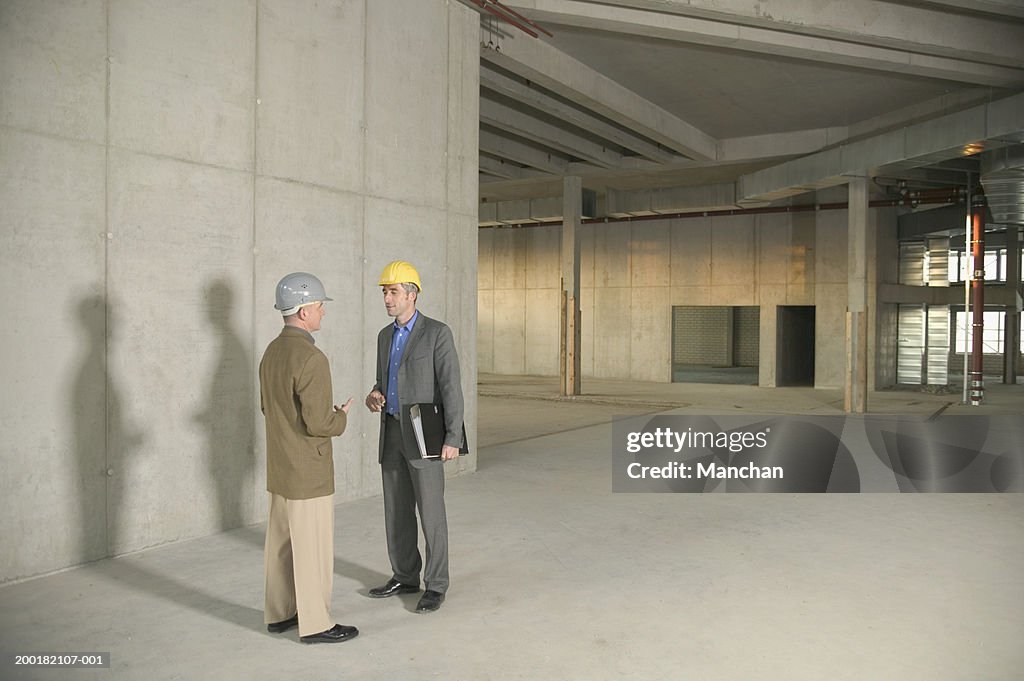 Two businessmen wearing hard hats in building