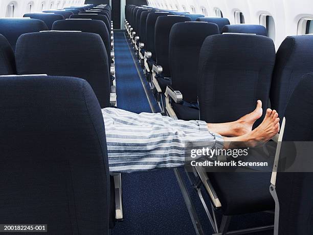 man lying on aeroplane seats, legs stretched across aisle, low section - jet lag stockfoto's en -beelden