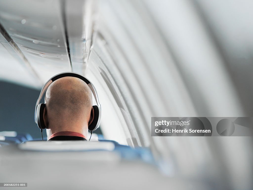 Businessman sitting on aeroplane seat, wearing headphones, rear view