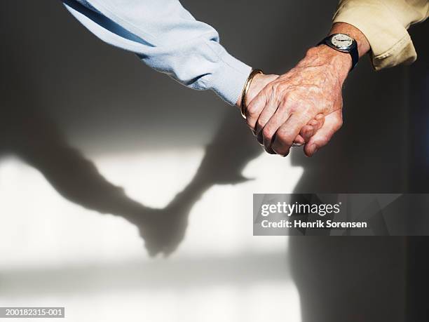 elderly couple holding hands, casting shadow on wall, close-up - holding hands close up stock-fotos und bilder