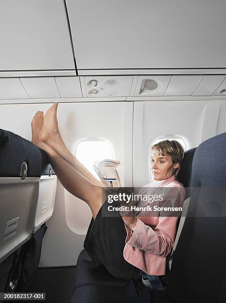 woman on aeroplane reading newspaper, resting feet on chair in front - barefoot stock pictures, royalty-free photos & images