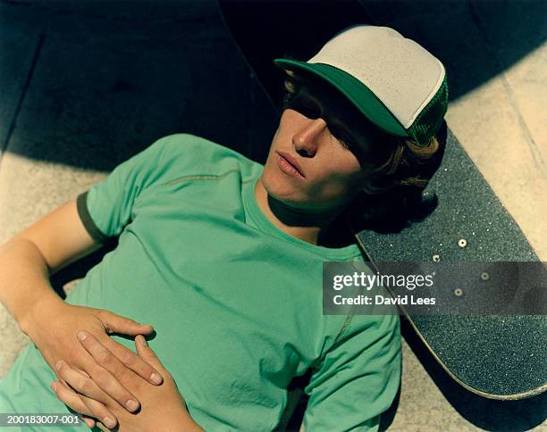 young man lying on ground, resting head on skateboard - mütze stock-fotos und bilder