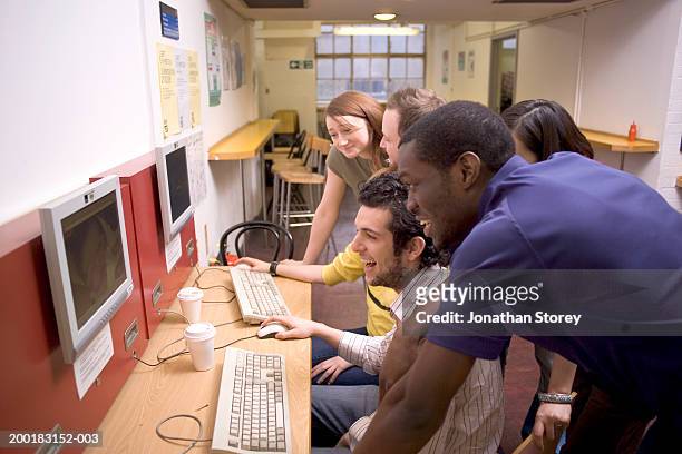 young adults looking at  computer in internet cafe, side view - internet cafe stock pictures, royalty-free photos & images
