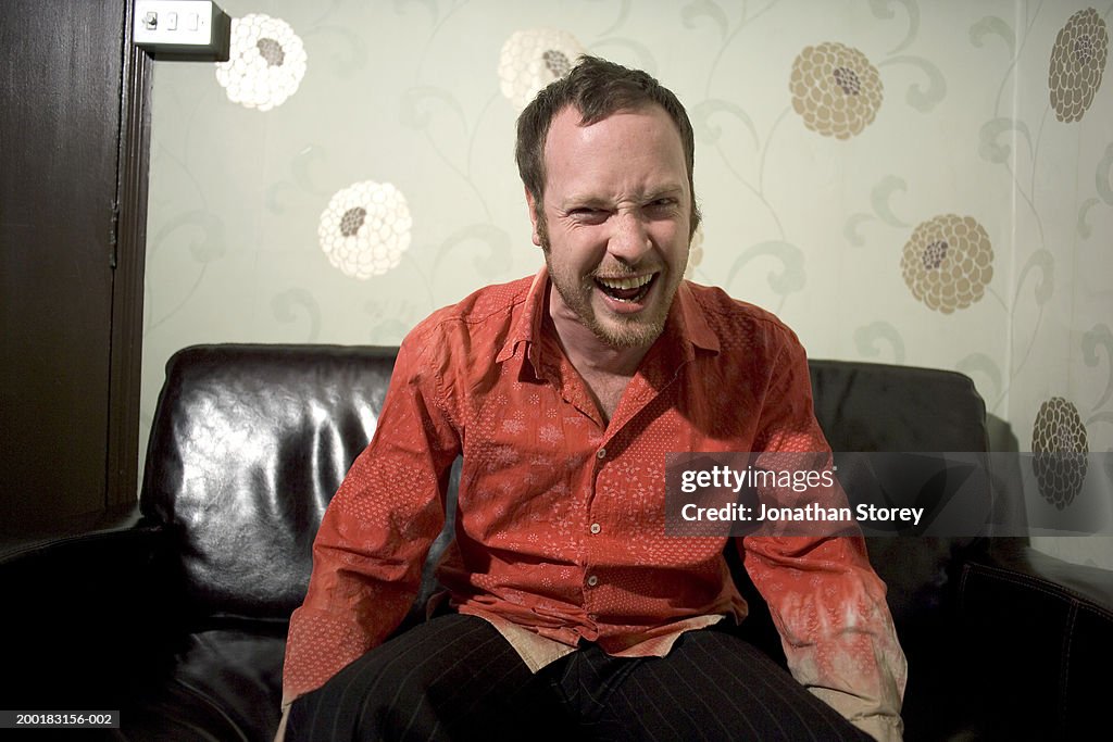 Young man sitting on sofa, laughing, portrait