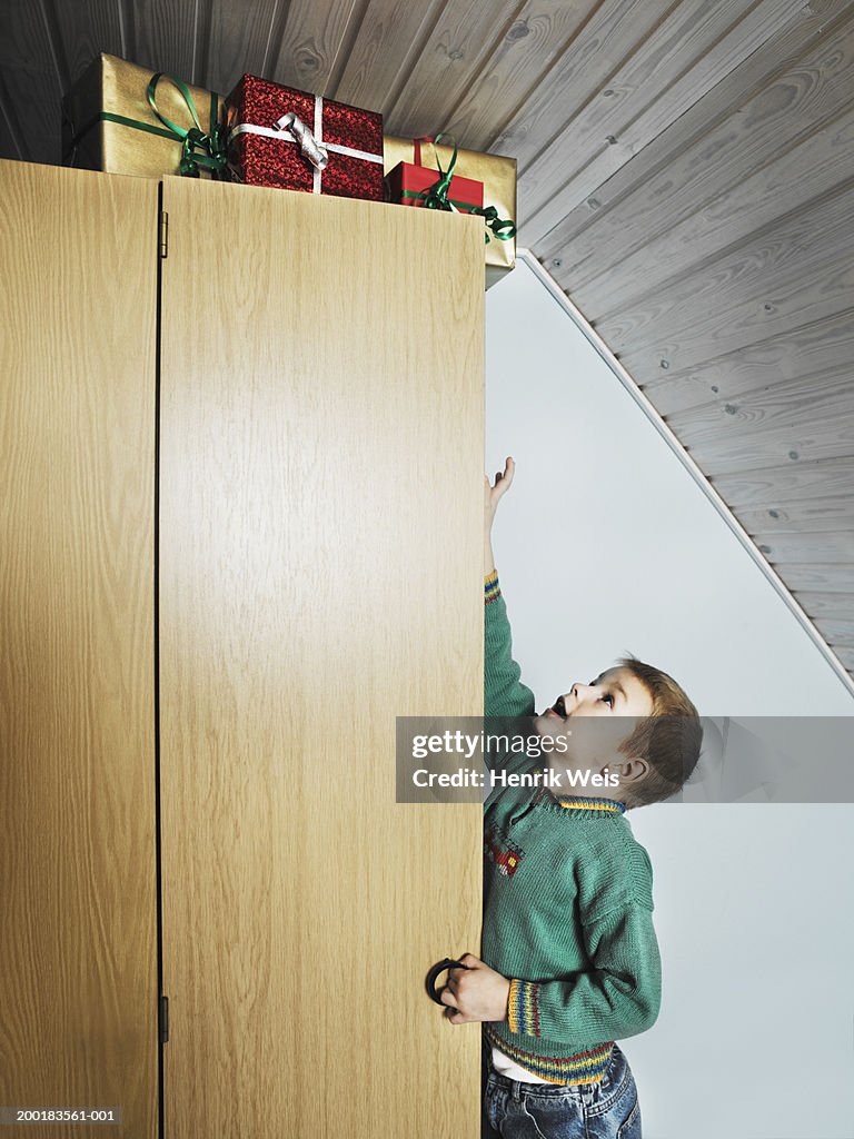 Boy (4-6) reaching for presents hidden on top of wardrobe