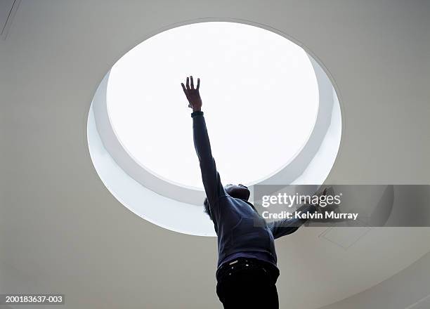 young man looking at skylight in ceiling, arms outstretched - skylight stock pictures, royalty-free photos & images