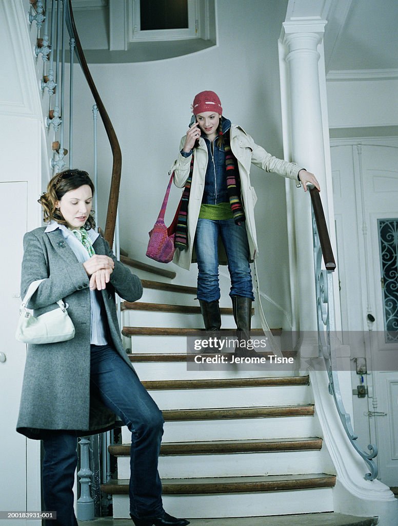 Young woman descending stairs, mother standing at bottom of stairs