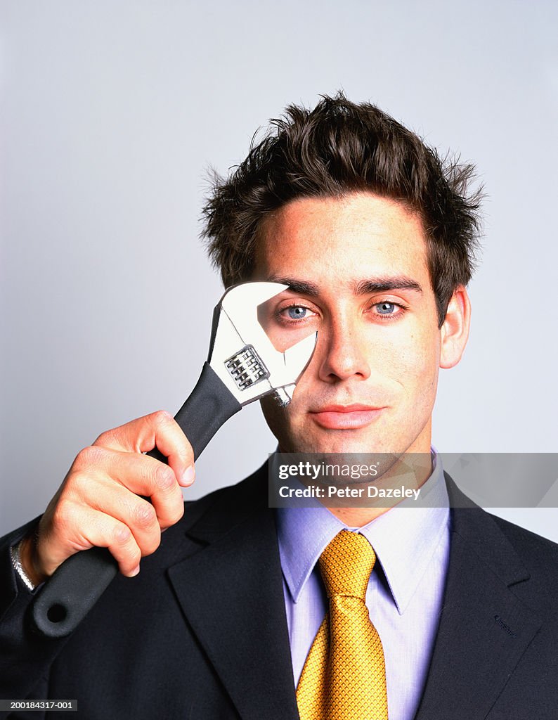 Young man holding adjustable spanner to eye, portrait