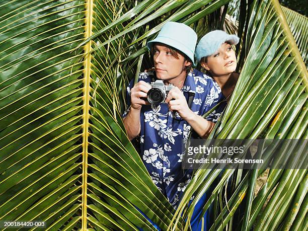 couple making way through jungle, standing between palm fronds - voyage15 photos et images de collection