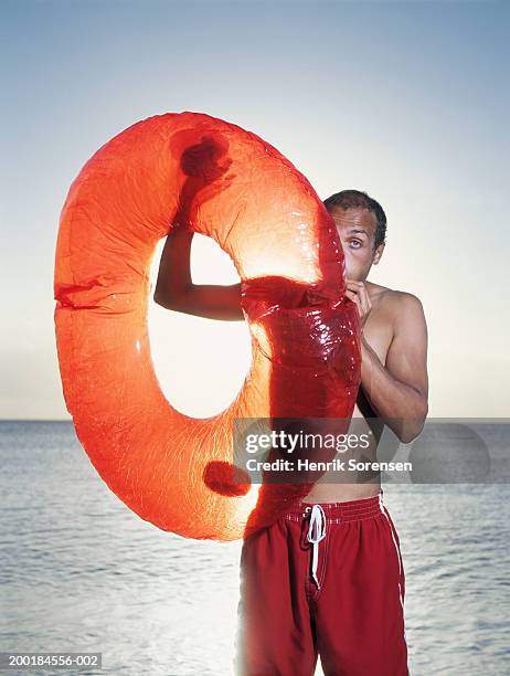 man on beach inflating rubber ring, portrait - inflatable ring stock-fotos und bilder