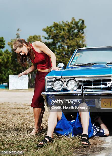 woman standing by man working underneath car, holding map - under skirt stock pictures, royalty-free photos & images