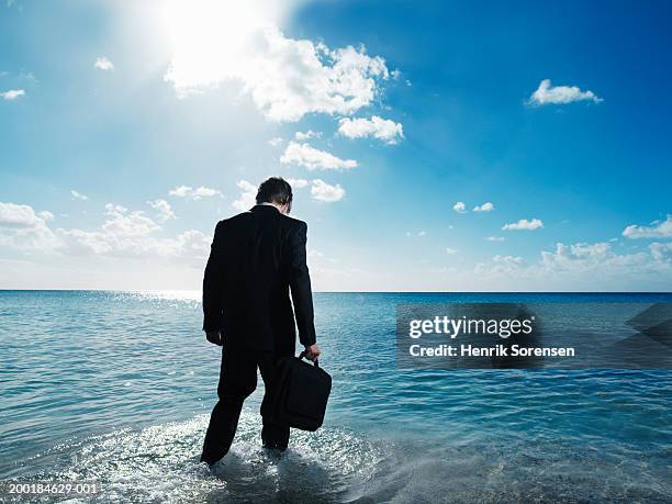 businessman walking in to sea, holding briefcase, rear view - ankle deep in water bildbanksfoton och bilder