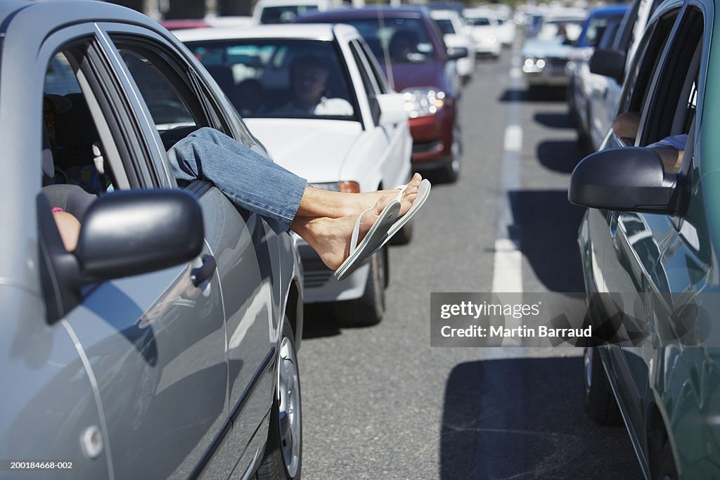 Mature man hanging feet outside of car window in traffic jam