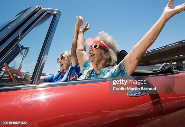 two senior women in convertible car, arms outstretched, side view - alleen seniore vrouwen stockfoto's en -beelden