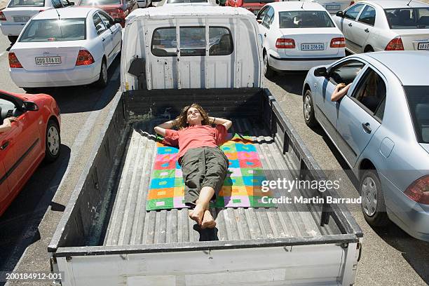 young man lying on towel in back of pickup truck amongst traffic jam - traffic jam lots of trucks stock pictures, royalty-free photos & images