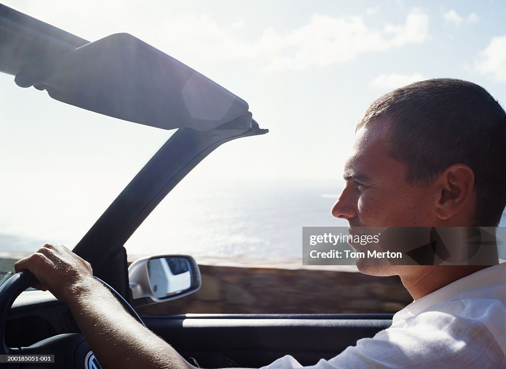 Man driving convertible car on coastal road, close-up