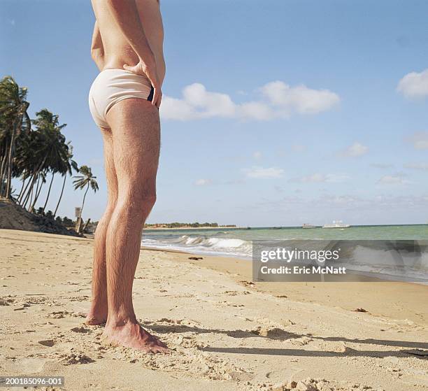 man standing on beach, arms akimbo, low section - slip de bain de compétition photos et images de collection