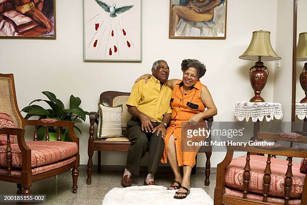 mature couple on chair in living room, smiling - gray hair couple stock pictures, royalty-free photos & images