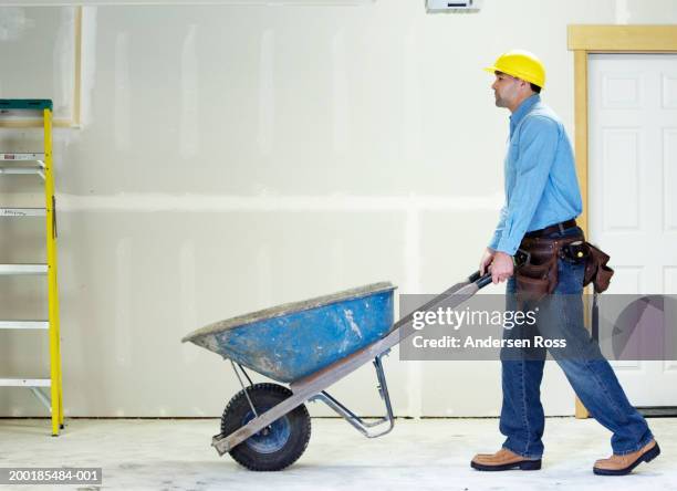 man pushing wheelbarrow on construction site, side view - wheelbarrow stock pictures, royalty-free photos & images