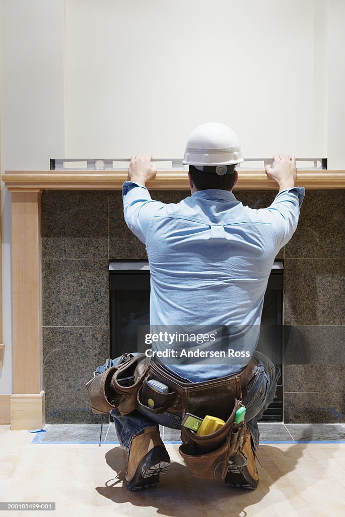 Man using level across top of mantelpiece, rear view